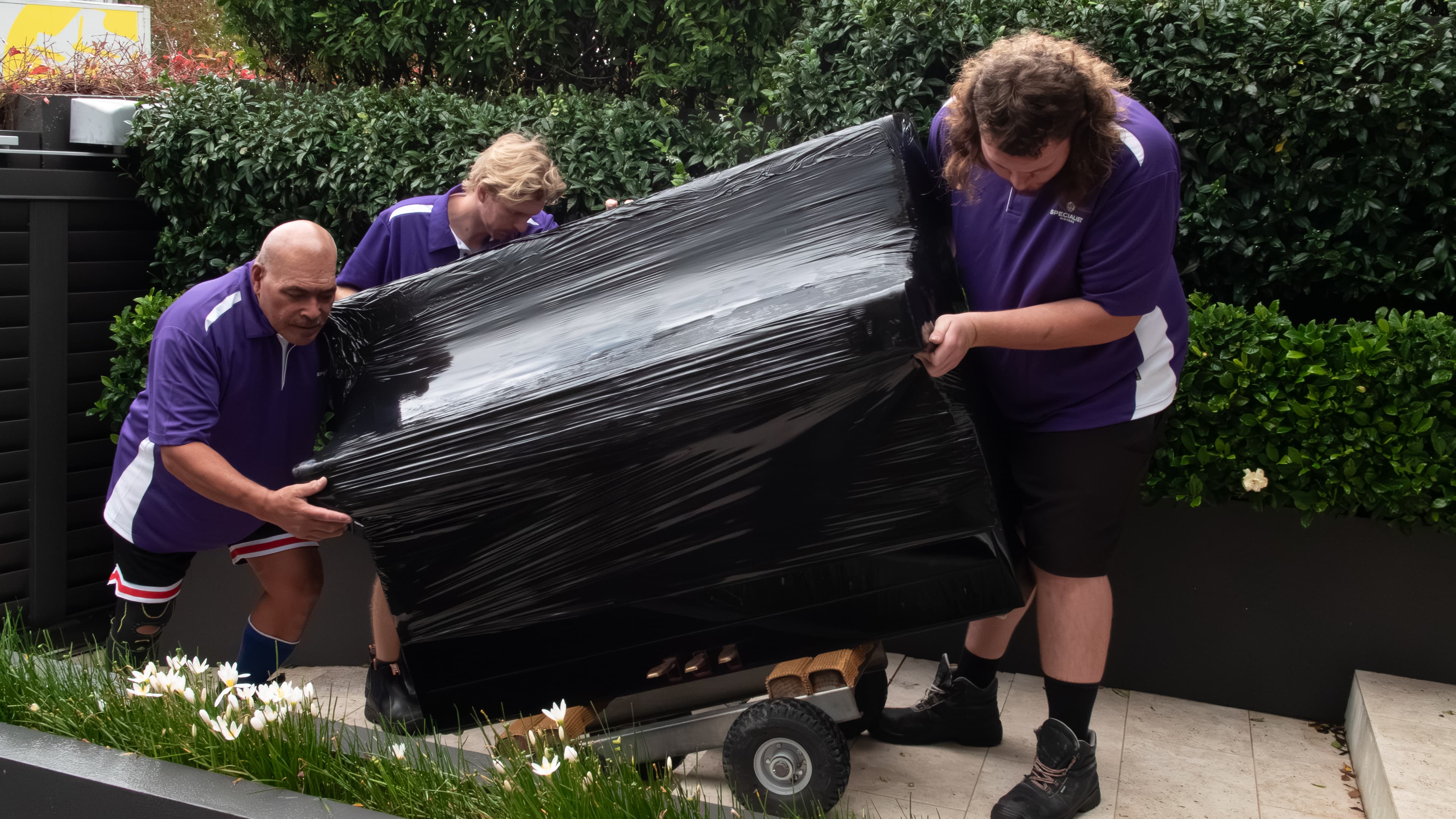 Two movers walking a wrapped upright piano on a dolly